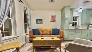 Ein Wohnzimmer mit einer Couch, einem Couchtisch und zwei Sesseln. Es gibt eine Küchenzeile mit Schränken und einem Spülbecken.