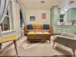 A living room with a sofa, coffee table, and two chairs. There is a kitchen area with cabinets and a sink. - Free Golf Cart | 1 Mi to Downtown & Beach (Ocean Springs)
