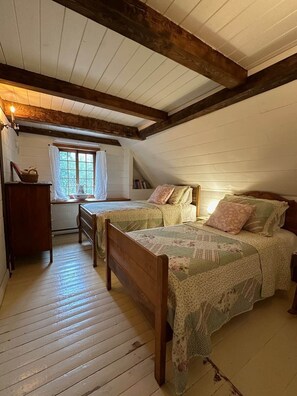 Ein gemütliches Schlafzimmer im Dachgeschoss mit zwei hölzernen Betten, einer Holzkommode und einem Fenster mit Vorhängen.