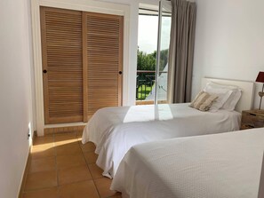 Quarto com duas camas, varanda e vista, e porta de correr.