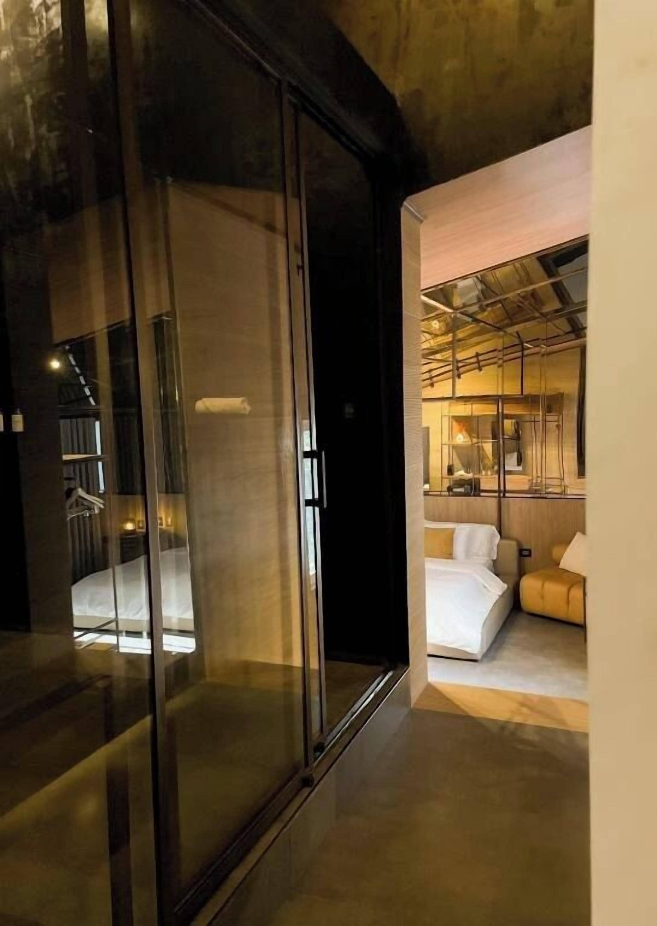 A modern interior with a glass door leading to a room with a bed and a sofa.