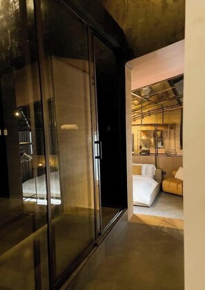 A modern interior with a glass door leading to a room with a bed and a sofa.