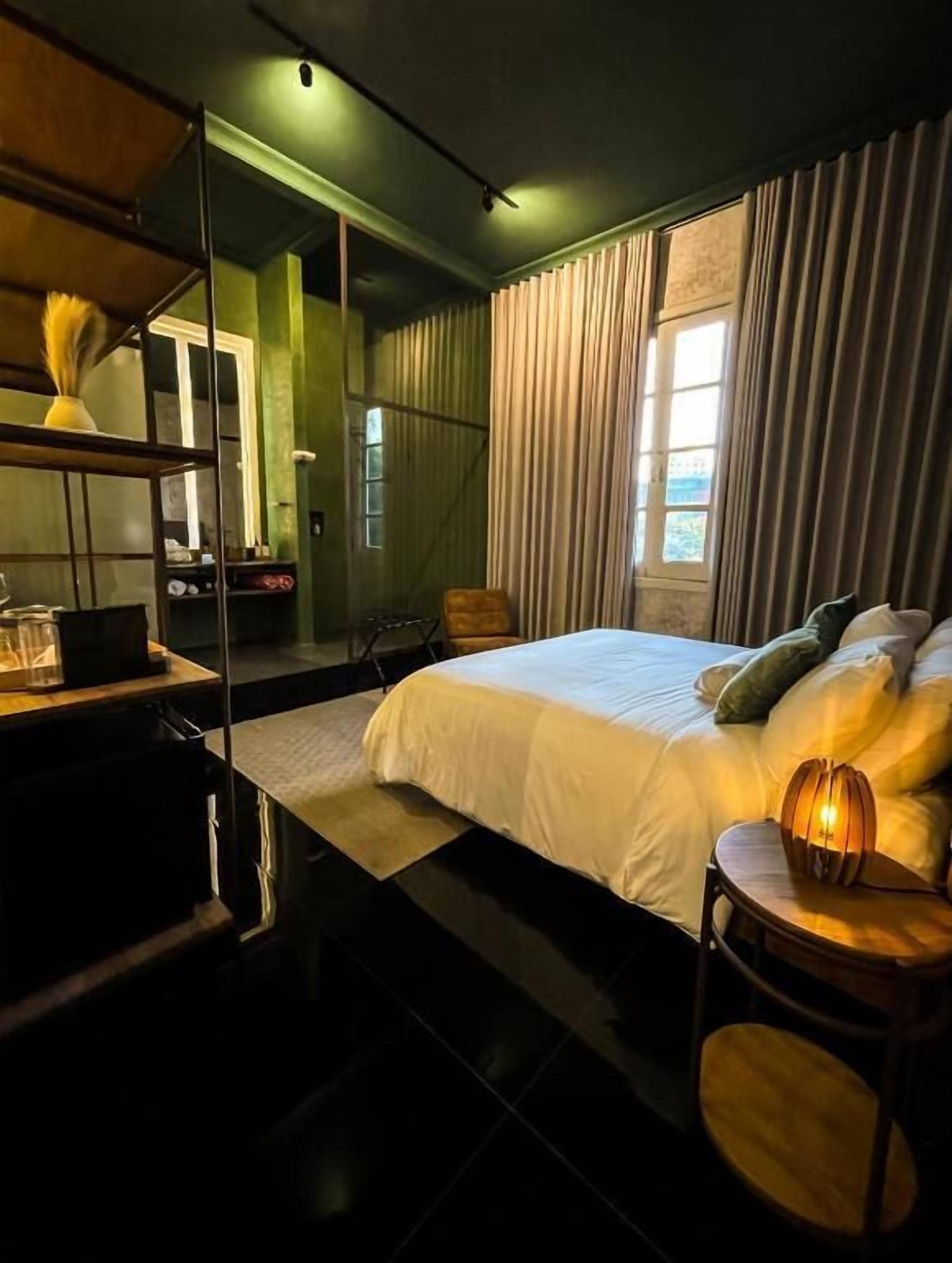 A hotel room with a bed, bedside table, lamp, and a large mirror.