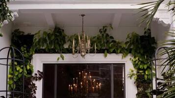 Ingresso di un hotel con pavimento a scacchi, un lampadario e verdeggiante vegetazione.