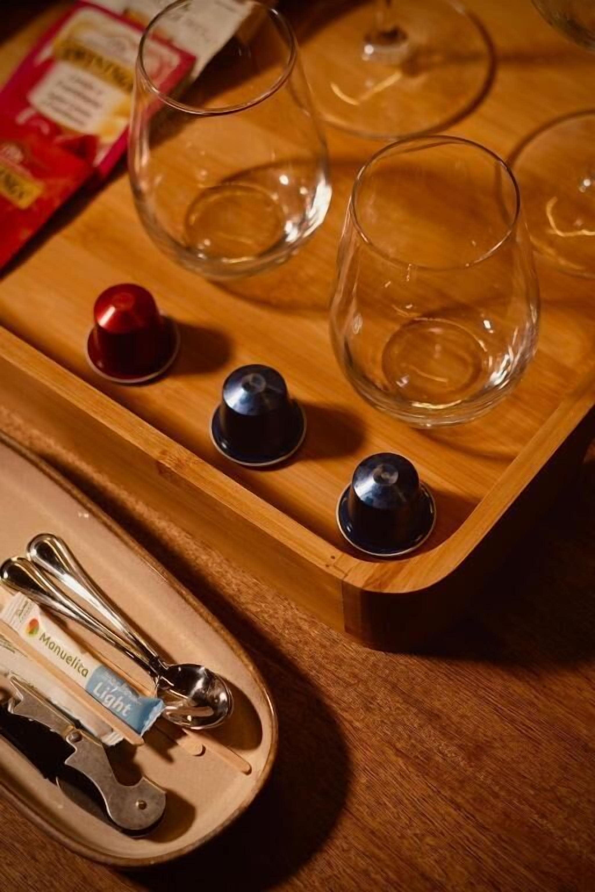 A wooden tray with three empty glasses and a pair of tongs on a table.