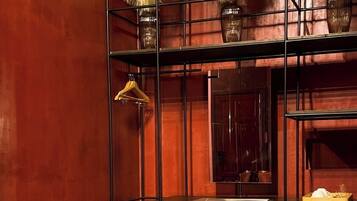 Um quarto com uma estante de metal preto, um banquinho bege e um pequeno eletrodoméstico no chão.