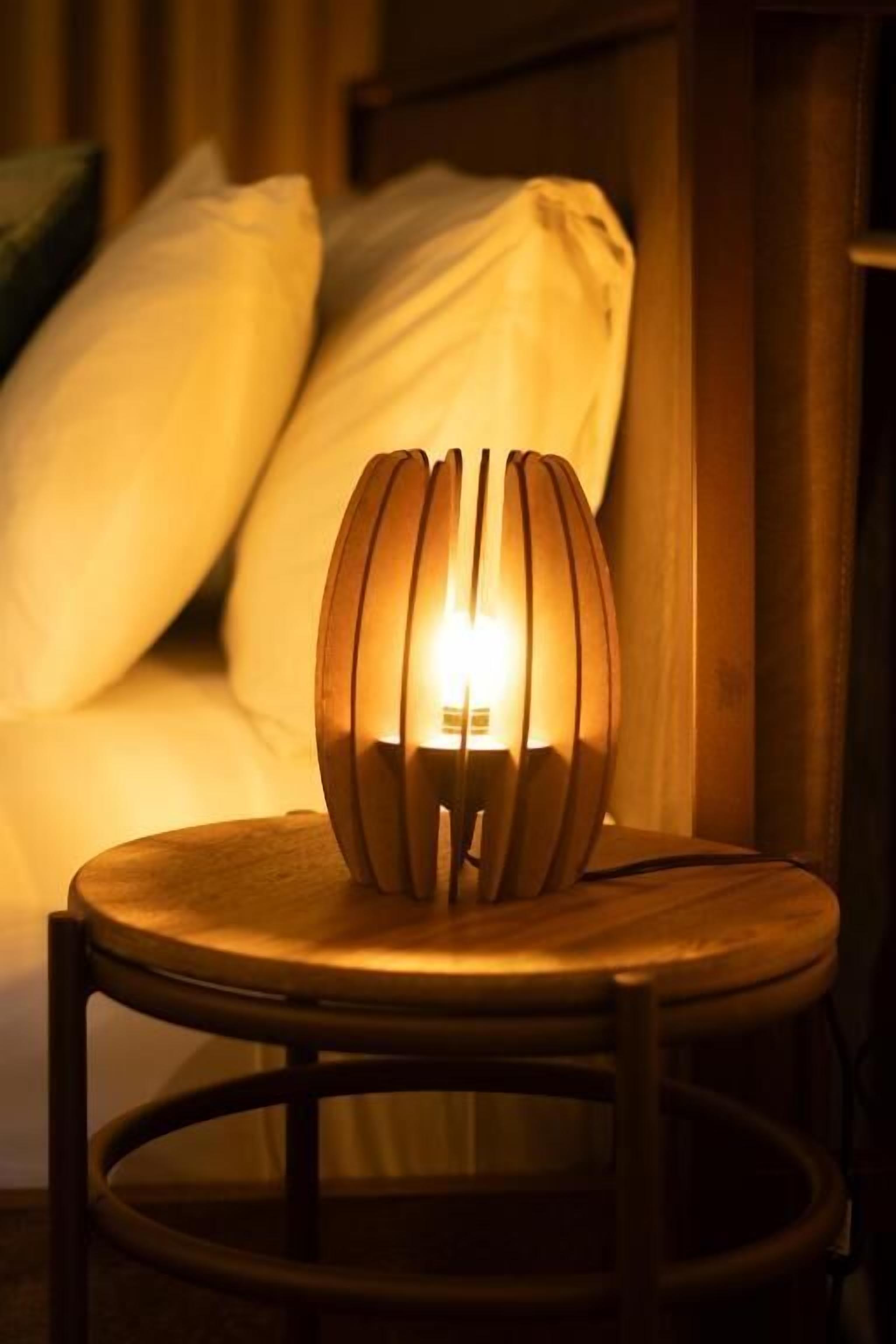 A bedside table with a lamp emitting a warm glow, a wooden chair, and a bed with pillows.