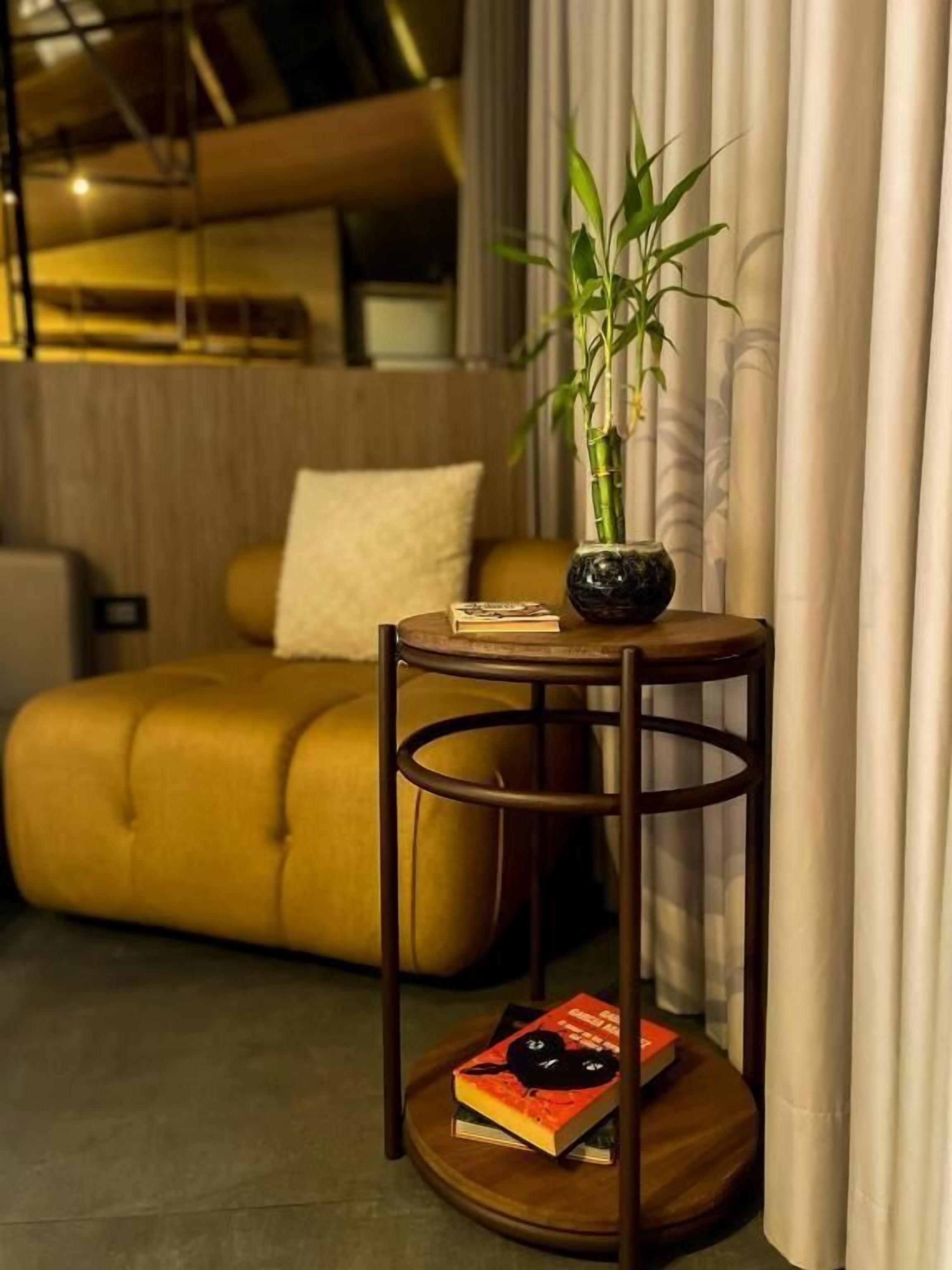 A round wooden table with a black vase containing a bamboo plant, a book, and a small black object.