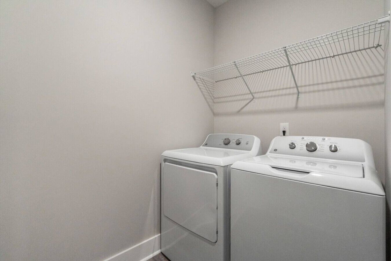A laundry room with two white stacked washer and dryer units, a metal drying rack, and a white wall.