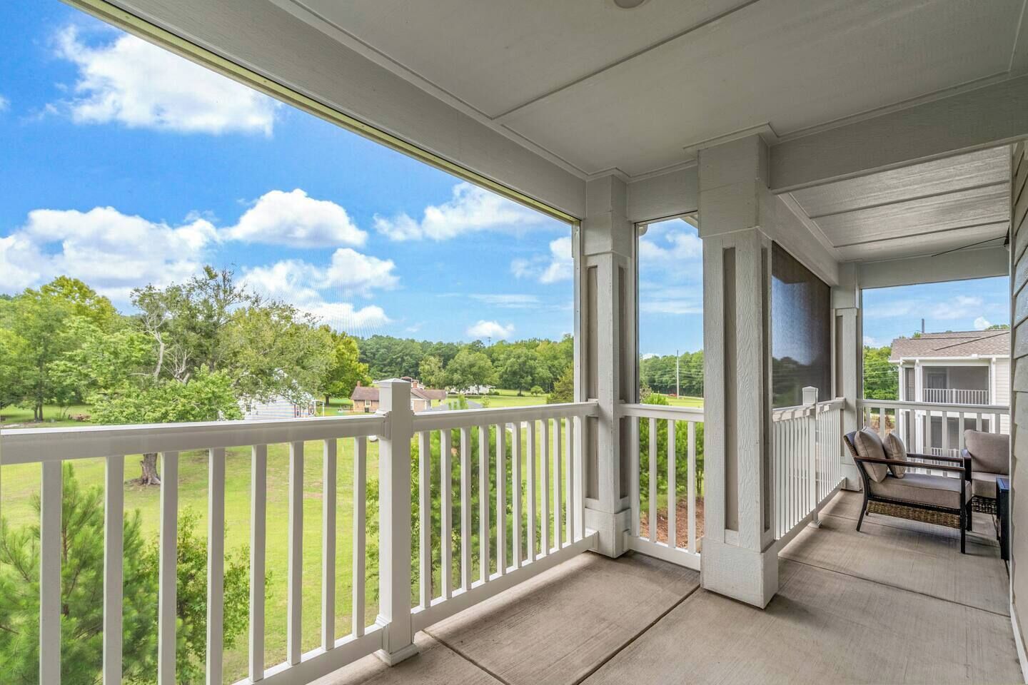 A covered porch with a view of a green landscape and a house in the distance.