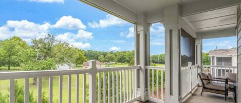 A covered porch with a view of a green landscape and a house in the distance.