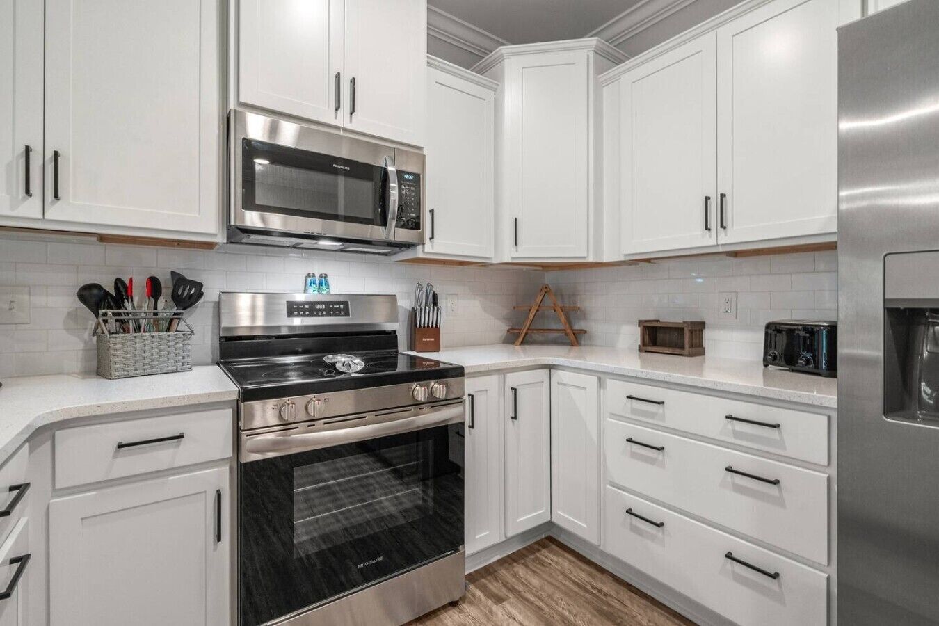 A kitchen with white cabinets, a stainless steel microwave, a stove, and a refrigerator.