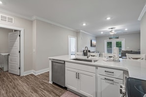 A modern kitchen with a dishwasher, a sink, and a dining area with chairs. - Brand NEW Calabash Condo (Calabash)