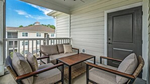 A covered porch with a table and chairs, a ceiling fan, and a view of neighboring buildings. - Brand NEW Calabash Condo (Calabash)