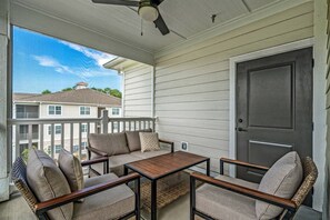 A covered porch with a table and chairs, a ceiling fan, and a view of neighboring buildings. - Brand NEW Calabash Condo (Calabash)