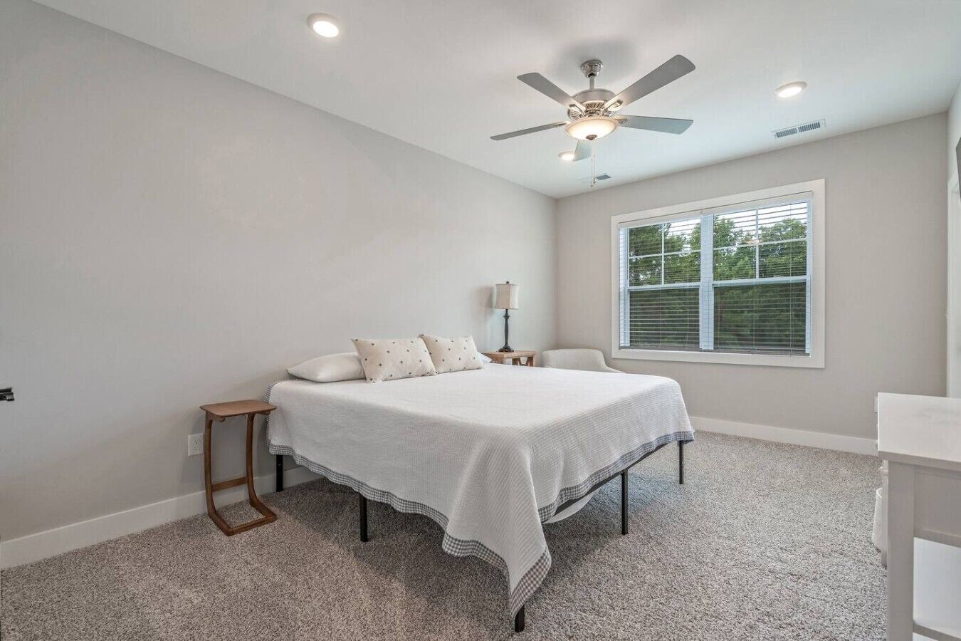 A bedroom with a bed, a nightstand, a lamp, a ceiling fan, and a window with blinds.