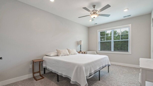 A bedroom with a bed, a nightstand, a lamp, a ceiling fan, and a window with blinds. - Brand NEW Calabash Condo (Calabash)
