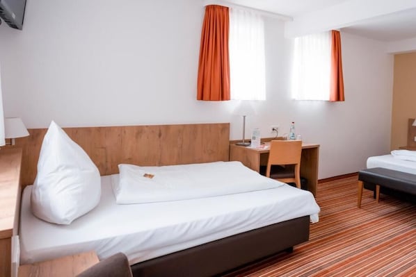 A hotel room with a bed, a desk, a chair, and a small table.