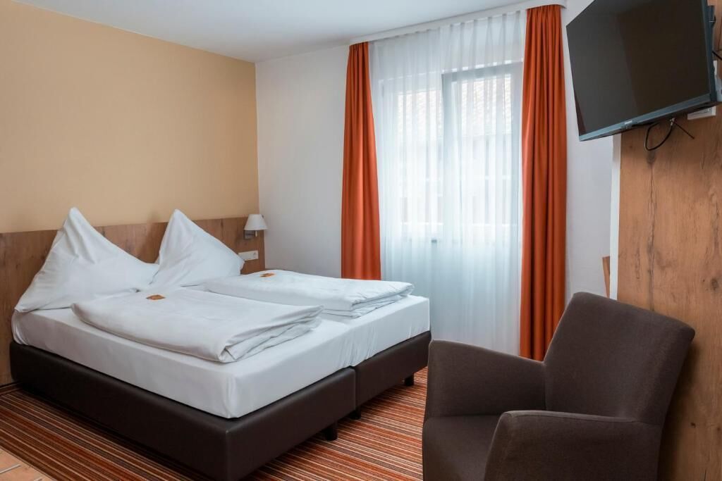 Een hotelkamer met een bed, een stoel, een televisie en gordijnen.