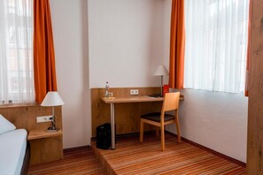 A hotel room with a bed, a desk, a chair, a lamp, and a window with curtains.