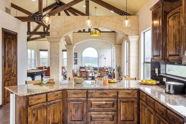 A spacious kitchen with a large island, wooden cabinets, and a stone archway leading to a dining area.