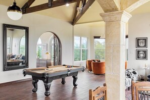 A pool table in a room with a high ceiling, large windows, and a stone column.
