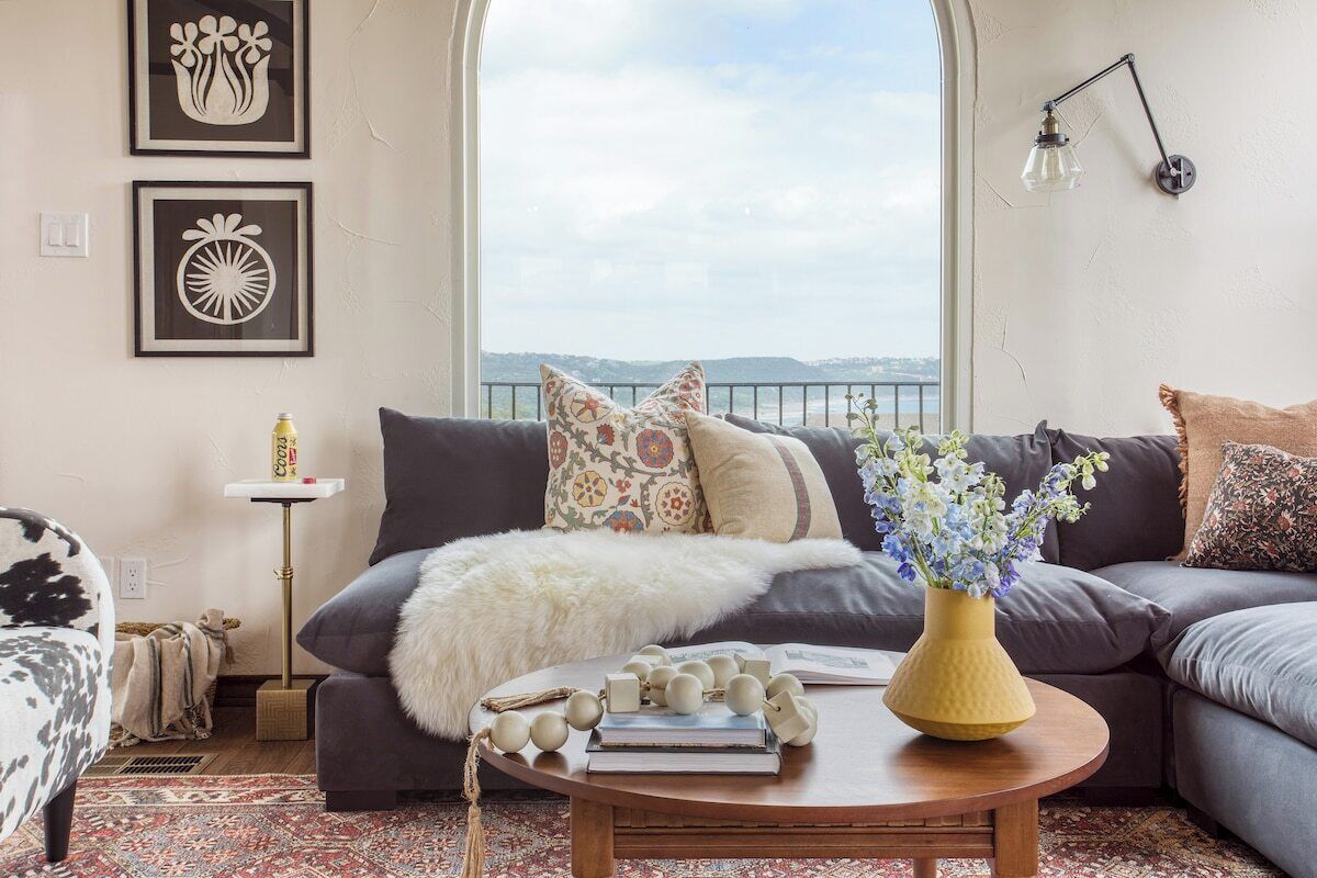 A living room with a sofa, a coffee table with decorative items, a view through a window, and a wall-mounted lamp.
