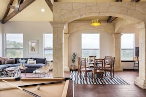 A spacious living room with a pool table, comfortable seating, and large windows offering a view.