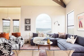 A cozy living room with a sectional sofa, a coffee table, and a view through an arched window.