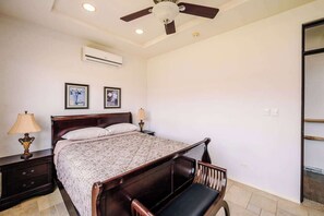 A bedroom with a bed, nightstands, a ceiling fan, and wall-mounted air conditioning. - Ocean & Mountain Views, Pool in Playa Ocotal (Playas del Coco)