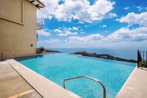 A clear blue swimming pool with a view of the sea and a building with a balcony. - Ocean & Mountain Views, Pool in Playa Ocotal (Playas del Coco)