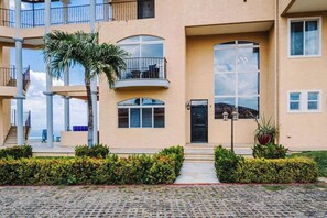 A multi-story building with balconies, a palm tree, and a paved courtyard. - Ocean & Mountain Views, Pool in Playa Ocotal (Playas del Coco)