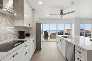 A modern kitchen with white cabinetry, a black stove, and a view to an outdoor patio. - Ocean & Mountain Views, Pool in Playa Ocotal (Playas del Coco)