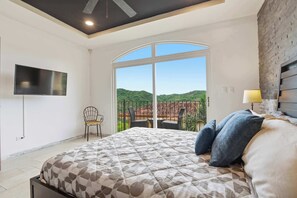A bedroom with a bed, a TV, a chair, and a balcony with a view of the hills. - Ocean & Mountain Views, Pool in Playa Ocotal (Playas del Coco)