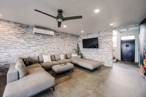 Un saló modern amb un sofà modular, un ventilador de sostre i un televisió de pantalla plana penjada a la paret.