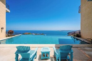 An infinity pool with a view of the ocean, surrounded by light blue chairs and a small table. - Ocean & Mountain Views, Pool in Playa Ocotal (Playas del Coco)