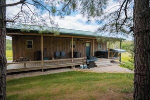 Eine Holzhütte mit Veranda, Sitzgelegenheiten im Freien und Grillplatz.
