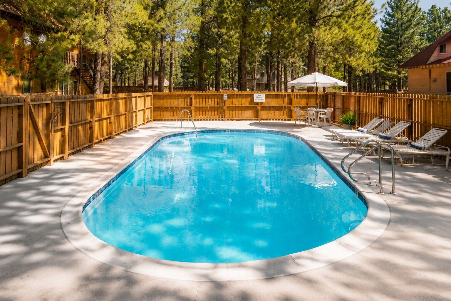 Piscina con valla de madera, sillas de descanso y una sombrilla.