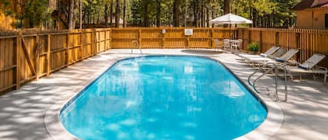 A swimming pool with a wooden fence, lounge chairs, and a small umbrella.