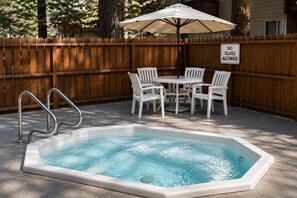 Un bain à remous entouré d’une clôture en bois, avec des chaises blanches et un panneau indiquant « VERRE INTERDIT ».