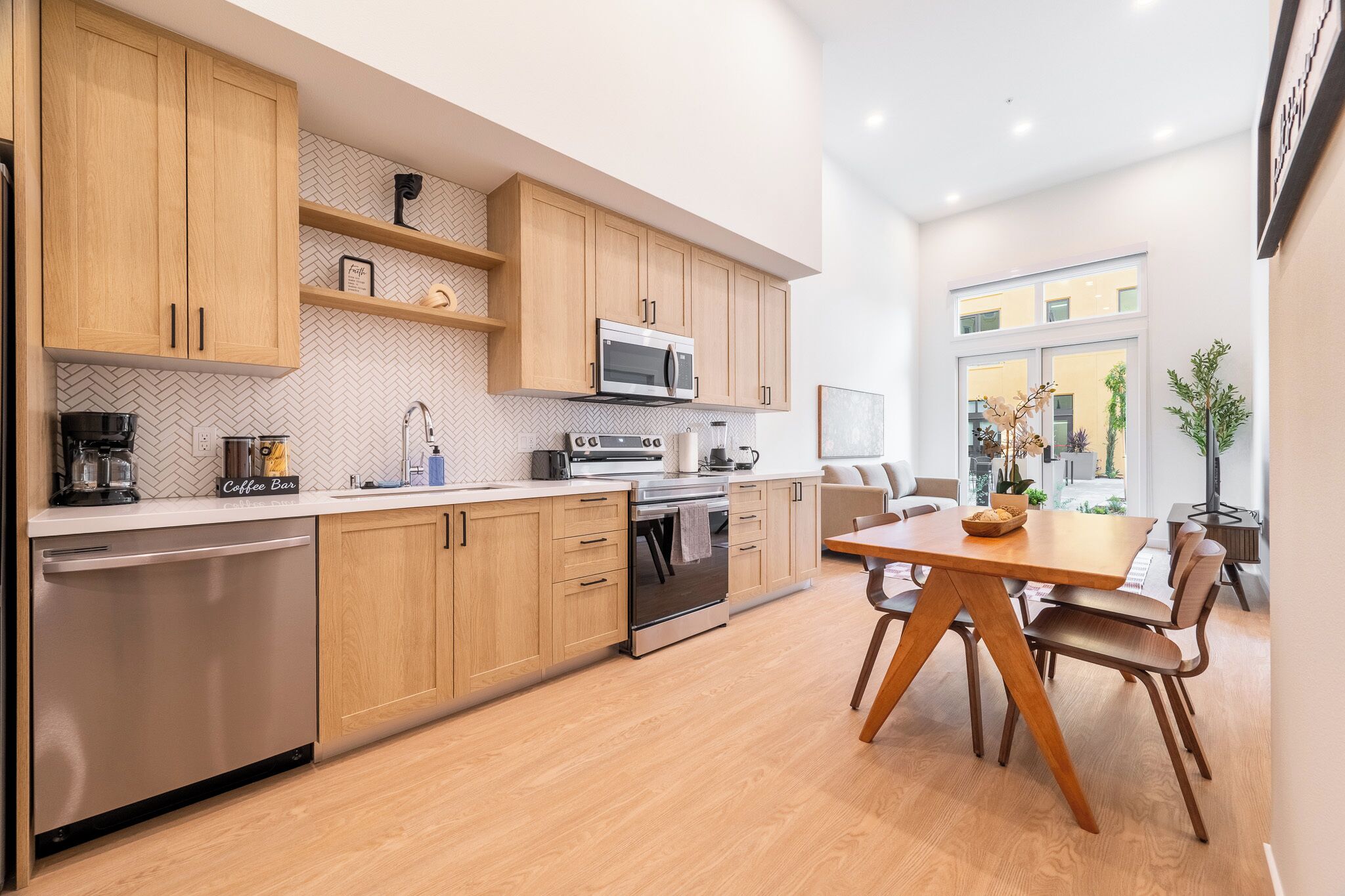 Una cocina moderna con armarios de madera, lavavajillas de acero inoxidable, horno empotrado y una barra para café.