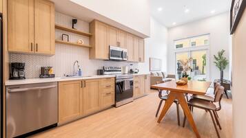 Una cocina moderna con armarios de madera, lavavajillas de acero inoxidable, horno empotrado y una barra para café.