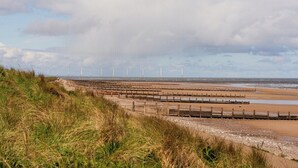 Eine Küstenlandschaft mit Windkraftanlagen, einem Sandstrand und einem Holzzaun.