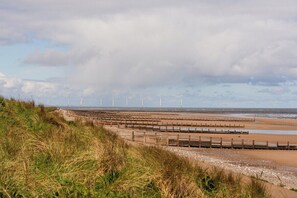 Eine Küstenlandschaft mit Windkraftanlagen, einem Sandstrand und einem Holzzaun.