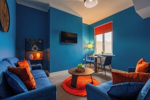 A living room with a blue sofa set, a round coffee table, and a television on the wall. - Cozy Blue Ember Stay | Work friendly 4BR+Sleeps 7 (Redcar and Cleveland)