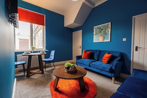 Una habitación con pared azul, sofá azul, una mesita de centro redonda de madera y una alfombra roja.
