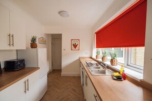 Una cocina con armarios blancos, encimera de madera, un tostador, un fregadero y una ventana con persiana roja.