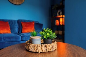 Una mesa redonda de madera con una bandeja tejida que contiene una planta, una vela y un adorno.