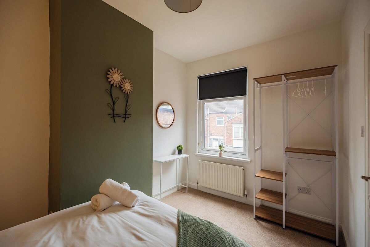 A bedroom with a bed, a radiator, a window with a view, a wardrobe, and a wall decoration.
