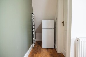 A narrow hallway with a white refrigerator, a radiator, and a door. - The Alfred 4BR Suite in Redcar | Sleeps 7+Parking (Redcar and Cleveland)